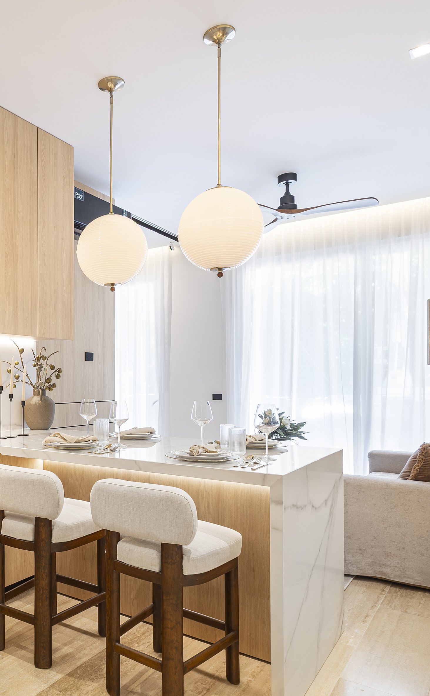 Two white ribbed glass globe pendants with brass rods over a marble island