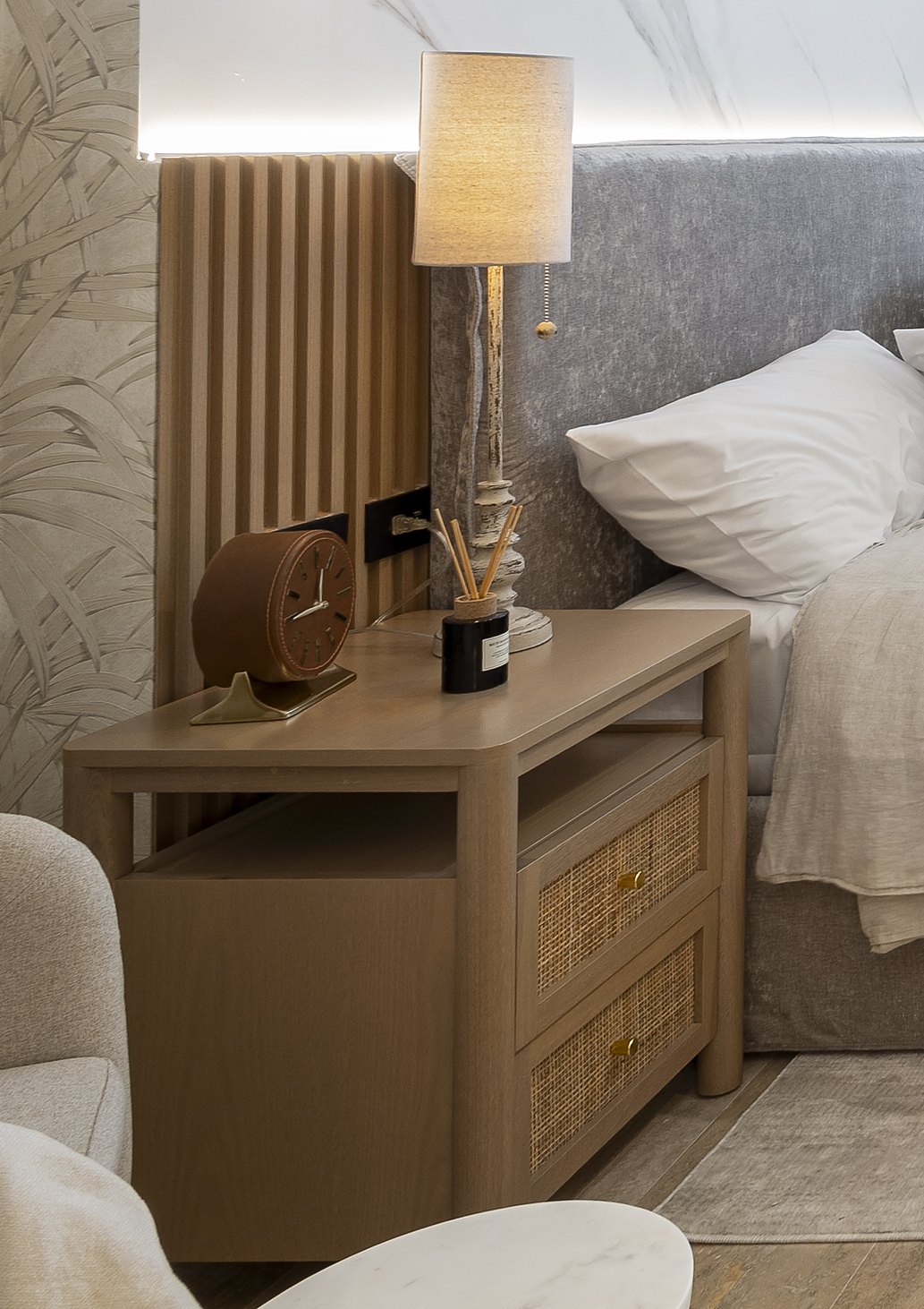 Light oak nightstand with rattan drawers and a candlestick lamp