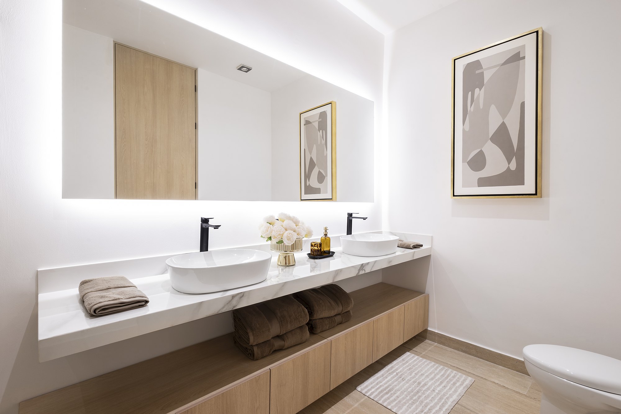 Floating marble vanity with two vessel sinks, black faucets and a backlit mirror